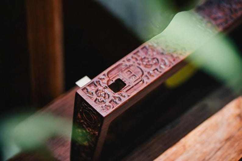 May include: A close-up of a wooden incense burner with intricate carvings. The burner has a small opening in the center for incense sticks.