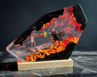 May include: A resin sculpture featuring two miniature figures in a duel, encased in a transparent block with black and fiery orange swirling patterns. The figures stand on a textured base, connected by a colorful light effect, mounted on a wood stand.