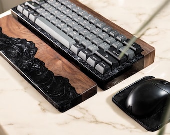 Puede incluir: Un teclado mecánico negro y gris con un reposamuñecas de madera de nogal y resina negra. Un ratón negro está sobre una alfombrilla de ratón de cuero negro.