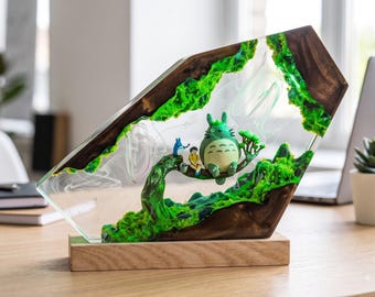 May include: A decorative resin and wood sculpture featuring a large gray Totoro figure, a small blue Totoro, and a human character sitting on a tree branch. The piece includes vibrant green moss-like textures embedded within clear resin.