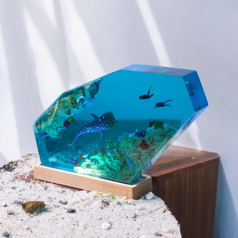 May include: A blue resin sculpture of a whale shark swimming in a coral reef. The sculpture is on a wooden base and is illuminated from within.