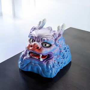 Pu&ograve; includere: Una scultura in ceramica blu e viola di una creatura mitologica con un'espressione feroce. La scultura ha una superficie testurizzata ed &egrave; decorata con dettagli intricati.