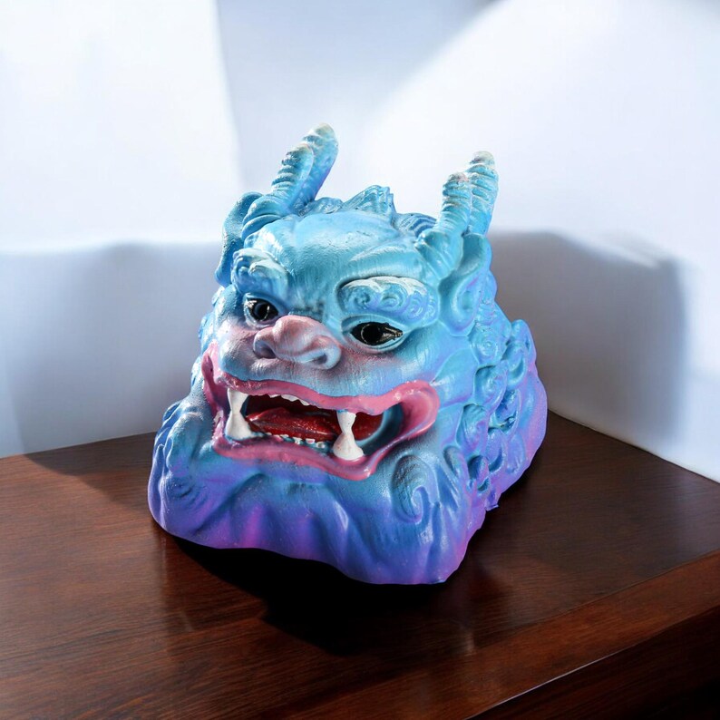 Pu&ograve; includere: Una scultura in ceramica blu e viola di una creatura mitologica con un'espressione feroce. La creatura ha denti grandi e affilati e corna.