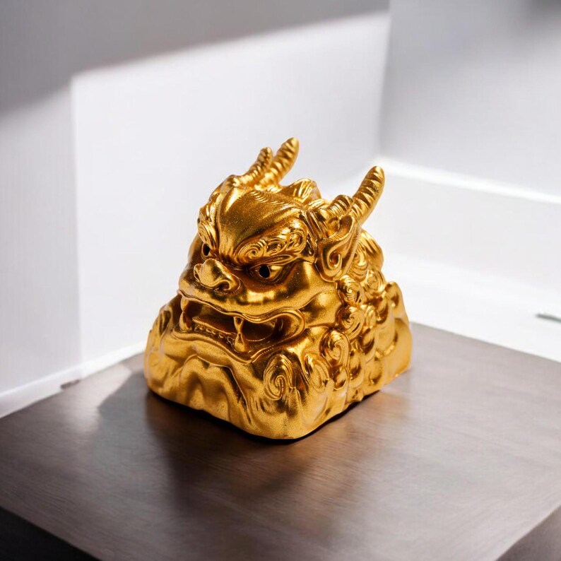Pu&ograve; includere: Una statuetta decorativa dorata e dettagliata di una creatura mitica simile a un leone con corna e un'espressione feroce. La statuetta &egrave; realizzata in un materiale liscio e lucido e ha una superficie testurizzata.