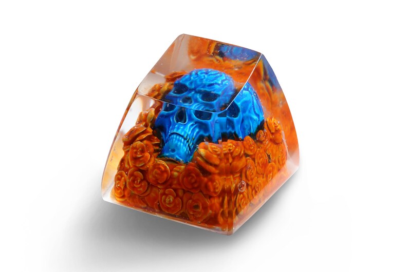 May include: A blue skull resin keycap with orange floral details encased in clear resin.