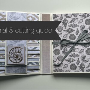Puede incluir: Un tutorial y una gu&iacute;a de corte para un &aacute;lbum de recortes con tem&aacute;tica de conchas marinas. El &aacute;lbum est&aacute; hecho con papel estampado, tela y cinta. La portada presenta un patr&oacute;n de conchas marinas gris y blanco. El interior del &aacute;lbum presenta una variedad de patrones y texturas diferentes.