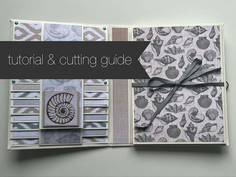 Puede incluir: Un tutorial y una gu&iacute;a de corte para un &aacute;lbum de recortes con tem&aacute;tica de conchas marinas. El &aacute;lbum est&aacute; hecho con papel estampado, tela y cinta. La portada presenta un patr&oacute;n de conchas marinas gris y blanco. El interior del &aacute;lbum presenta una variedad de patrones y texturas diferentes.