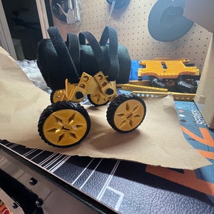 May include: A gold-colored toy vehicle with four wheels and black straps. The vehicle is made of plastic and has a Lego-like design.