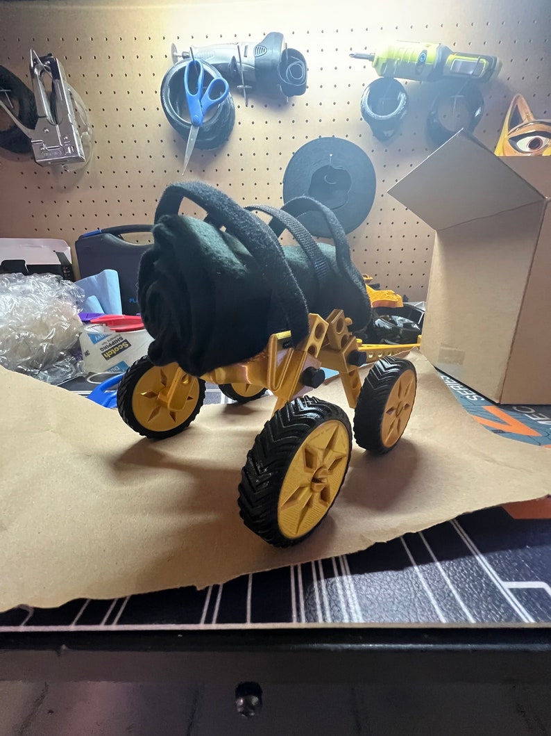 May include: A gold-colored, four-wheeled, all-terrain vehicle with black tires. The vehicle has a black fabric roll attached to the top.
