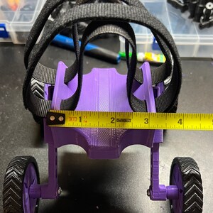 May include: Purple 3D printed toy car with black straps and wheels. The car is about 1 foot long and has a yellow tape measure across the front.