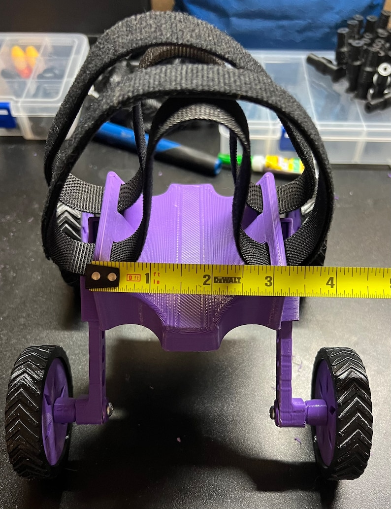 May include: Purple 3D printed toy car with black straps and wheels. The car is about 1 foot long and has a yellow tape measure across the front.