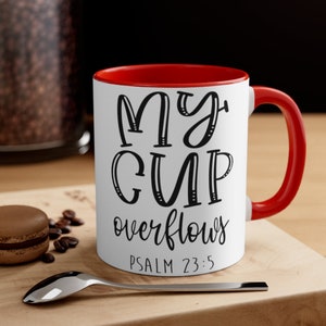 May include: White ceramic mug with a red rim and handle. The mug has black text that reads "My cup overflows" and "Psalm 23:5".