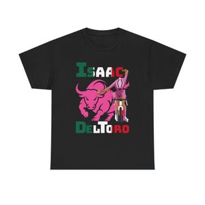 Puede incluir: Camiseta negra con un gráfico de toro rosa y el nombre "ISAAC DELTORO" en texto verde y rojo. Una figura de ciclista se representa junto al toro. El diseño incorpora elementos de la bandera mexicana.
