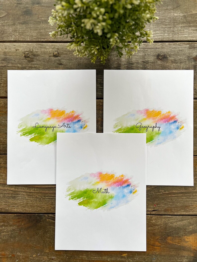 May include: Three white sheets of paper with colourful watercolour backgrounds. The top sheet says "Geography", the middle sheet says "Math", and the bottom sheet says "Language Arts".