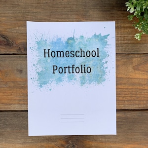 May include: A white sheet of paper with a blue watercolour splatter design. The text "Homeschool Portfolio" is printed in black at the top of the page. Three lines are drawn in black at the bottom of the page.
