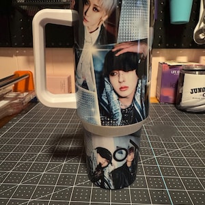 Puede incluir: Una taza de viaje blanca con un asa negra. La taza está cubierta con un collage de fotos de un grupo de personas. Las fotos son en blanco y negro y en color.