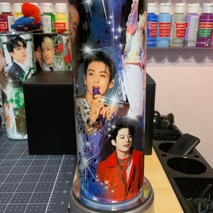 Pu&ograve; includere: Un bicchiere in acciaio inossidabile con un design colorato che presenta pi&ugrave; immagini di un cantante maschile. Il design include note musicali, stelle e uno sfondo blu e viola.