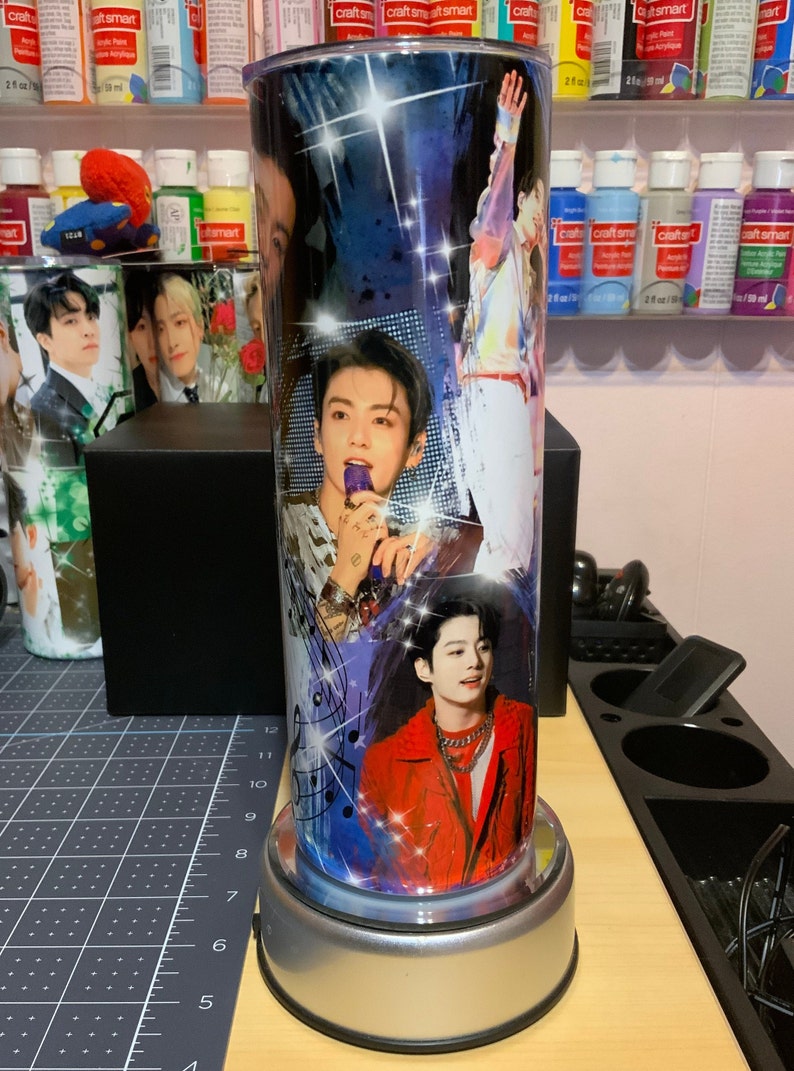 Pu&ograve; includere: Un bicchiere in acciaio inossidabile con un design colorato che presenta pi&ugrave; immagini di un cantante maschile. Il design include note musicali, stelle e uno sfondo blu e viola.