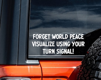 May include: Orange Jeep Wrangler with a black top and a spare tire. A white decal on the rear window reads: "FORGET WORLD PEACE VISUALIZE USING YOUR TURN SIGNAL!"