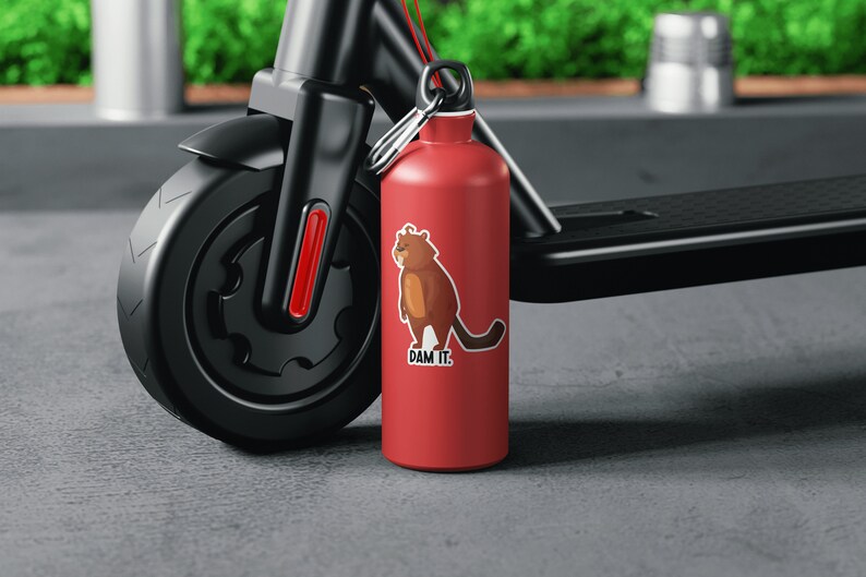 May include: A red water bottle with a black and brown cartoon animal sticker that says "DAM IT." The bottle is attached to a black electric scooter.