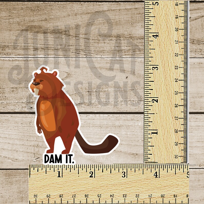May include: A cartoon beaver with a grumpy expression and large teeth stands on its hind legs with its tail behind it. The beaver is brown with a light orange belly. The text "DAM IT." is below the beaver.