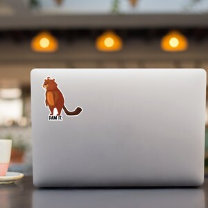 May include: A brown cartoon beaver with a grumpy expression stands on a laptop with the text "DAM IT."
