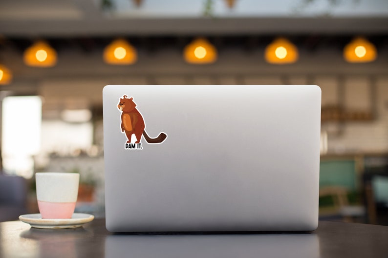 May include: A brown cartoon beaver with a grumpy expression stands on a laptop with the text "DAM IT."