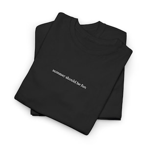 May include: Two black t-shirts are neatly folded and stacked. The phrase "summer should be fun" is printed in white, centered on the top shirt. The shirts are made of a soft material and are suitable for casual wear.