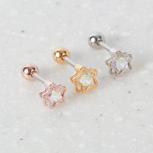 May include: Three star-shaped earrings with iridescent stones. The earrings are made of silver, gold, and rose gold.