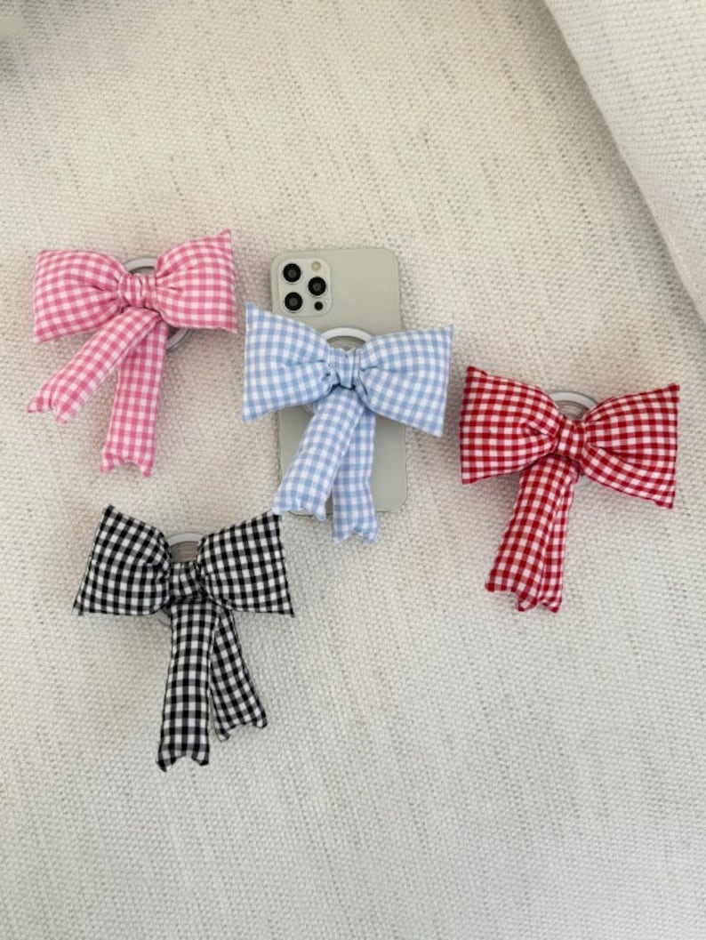 Puede incluir: Cuatro soportes para anillos de tel&eacute;fono con lazos de vichy de diferentes colores. Los lazos son rosa, azul, rojo y blanco y negro.
