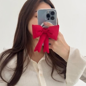 May include: A clear phone case with a red bow-shaped phone grip attached to the back.