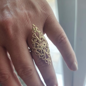 May include: A gold filigree ring with a delicate, intricate design. The ring is shaped like a teardrop and has a pointed top.