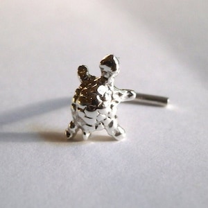 May include: Silver nose ring with a detailed turtle charm. The turtle is facing to the right and has a textured shell.