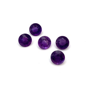 A lot of five round faceted natural amethyst loose gemstones. They measure 6.6mm and weigh a total of 5.08 carats. Deep purple in colour they are perfect for making a piece of jewellery. They are photographed from the top on a white background.