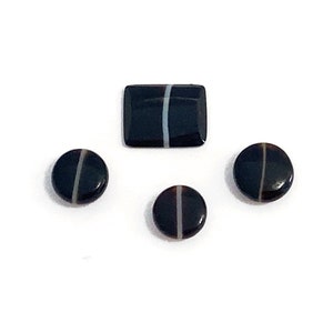 Four banded black and white onyx polished loose gemstones. They are mixed in shape and sizes. There are three round buttons and a cushion shaped stone with a central fine white band. Picture taken on a white background