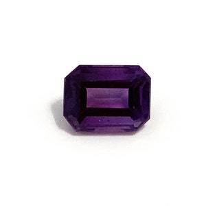 A deep rich purple octagon polished step cut faceted amethyst loose semi-precious gemstone. One single gemstone on a white background.