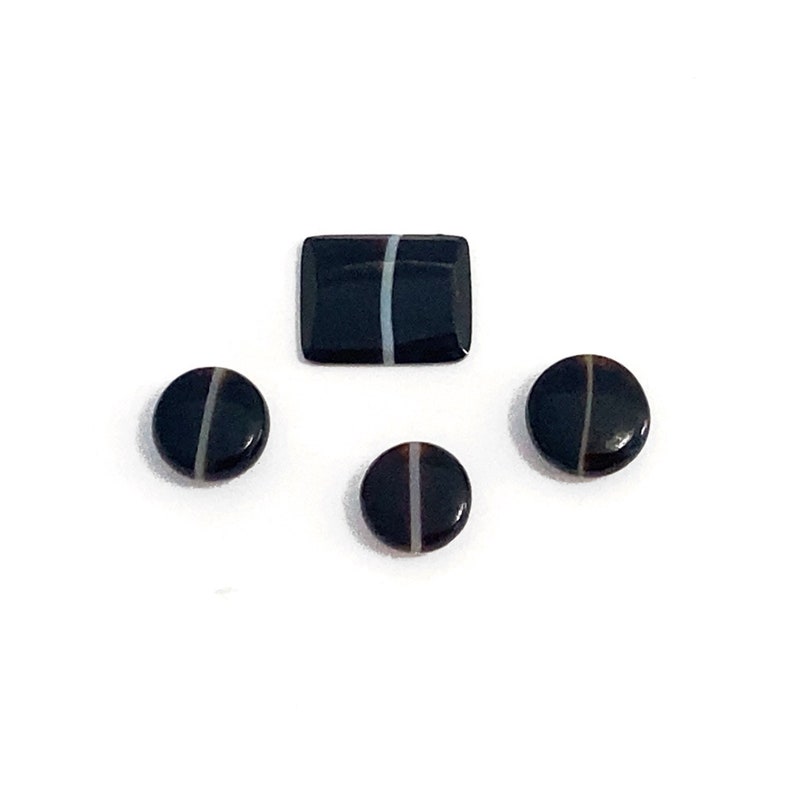 Four banded black and white onyx polished loose gemstones. They are mixed in shape and sizes. There are three round buttons and a cushion shaped stone with a central fine white band. Picture taken on a white background