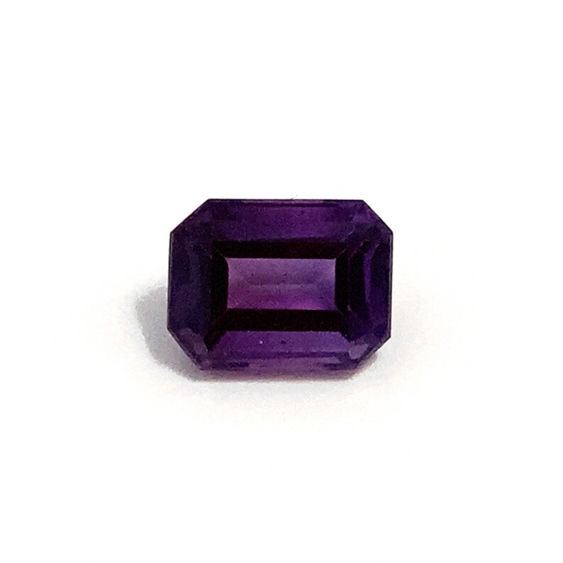 A deep rich purple octagon polished step cut faceted amethyst loose semi-precious gemstone. One single gemstone on a white background.