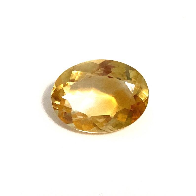 An oval deep yellow faceted citrine loose gemstone. It measures 16x12mm and weighs 7.45 carats. This pretty polished semi-precious loose stone would be ideal for making a piece of jewellery. Photographed on a white background.