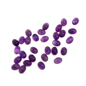 A collection of oval amethyst cabochon loose gemstones deep purple in colour. They measure 7x5mm and would be ideal for making a piece of jewellery. They have rounded polished tops and flat bases. Pictured on a white background.