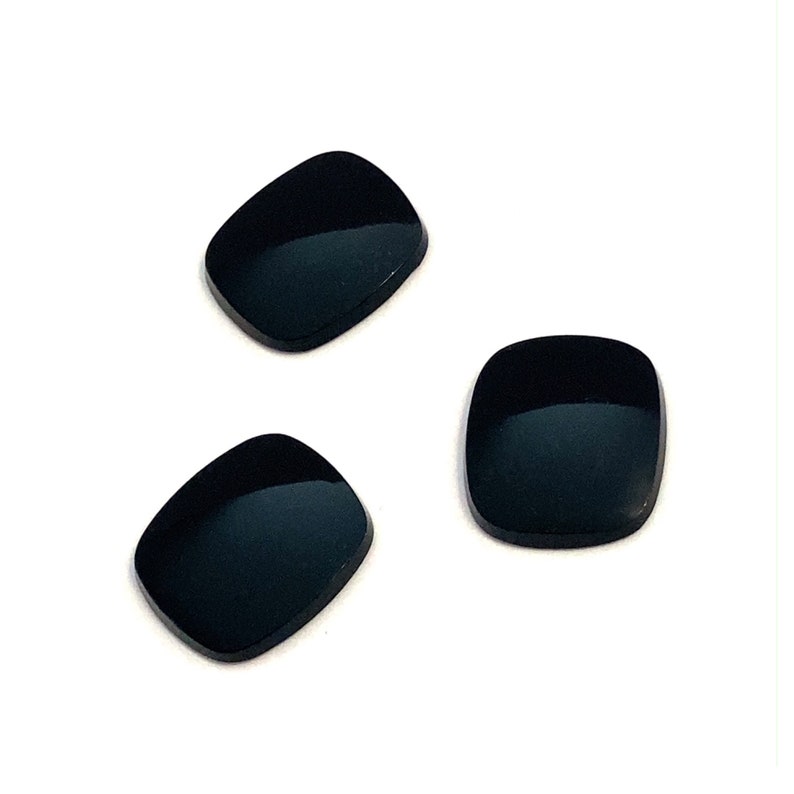 Three buff top black onyx polished loose flat gemstones. They are cushion shape with rounded edges ideal for making a signet ring or pair of cufflinks. The three stones are pictured in a group on a white background.