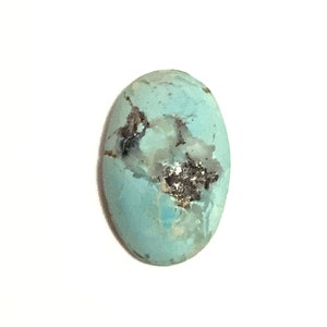 An oval shaped turquoise cabochon polished loose gemstone with a rounded domed top and a flat underside. It isa beautiful robins egg blue colour with dark brown mottled markings. Pictured from the top of the stone and on a white background