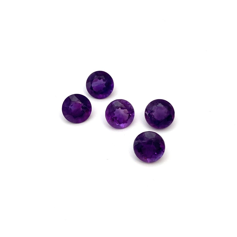 A lot of five round faceted natural amethyst loose gemstones. They measure 6.6mm and weigh a total of 5.08 carats. Deep purple in colour they are perfect for making a piece of jewellery. They are photographed from the top on a white background.