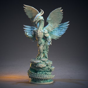 Op de afbeelding: Een groen en blauw miniatuur drakenbeeld met vleugels, staand op een rotsachtige basis. De draak heeft een lange nek en een scherpe snavel.