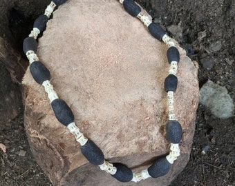 May include: A black and white beaded necklace with a tag that says "22". The necklace is made of round black beads and white bone-like beads.
