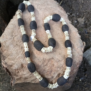 May include: A necklace made of black and white beads. The beads are strung together on a white cord. The necklace is lying on a piece of wood.