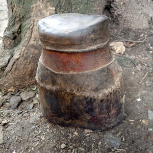 May include: A dark brown leather container with a red band and a textured surface. The container is slightly weathered and has a worn appearance.