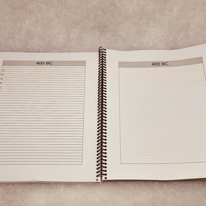 Puede incluir: Un cuaderno blanco de espiral con encuadernaci&oacute;n negra. El cuaderno tiene dos p&aacute;ginas abiertas, cada una con el texto "400 BC" en la parte superior. Las p&aacute;ginas est&aacute;n rayadas con l&iacute;neas grises.