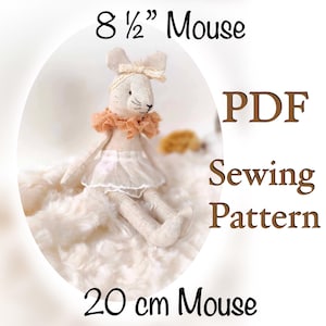 May include: PDF sewing pattern for an 8 1/2 inch mouse doll. The doll is made of beige fabric and has a pink bow on its head. The doll is sitting on a white fluffy surface.
