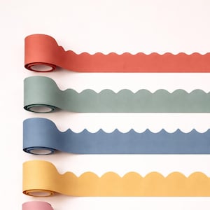 May include: A collection of six rolls of decorative paper tape in various colors. The colors include red, green, blue, yellow, pink, and burgundy. Each roll has a scalloped edge design, and the rolls are partially unrolled, showing the tape's texture.